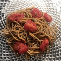 Die Spaghetti mit schwarzem Knoblauch und Burrata werden angerichtet, auf die Pasta mit der Soße kommen nun die Tomaten
