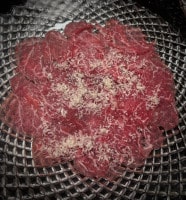 Die Carpaccio Scheiben werden auf dem Teller angerichtet und mit etwas Parmesan bestreut